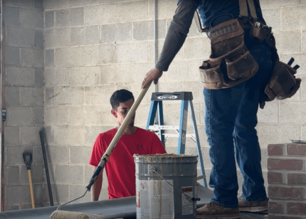 Two people painting a room: one using a roller, the other standing on a ladder. Paint and tools are visible.