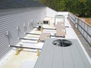Rooftop with HVAC units and metal railings against a corrugated building.