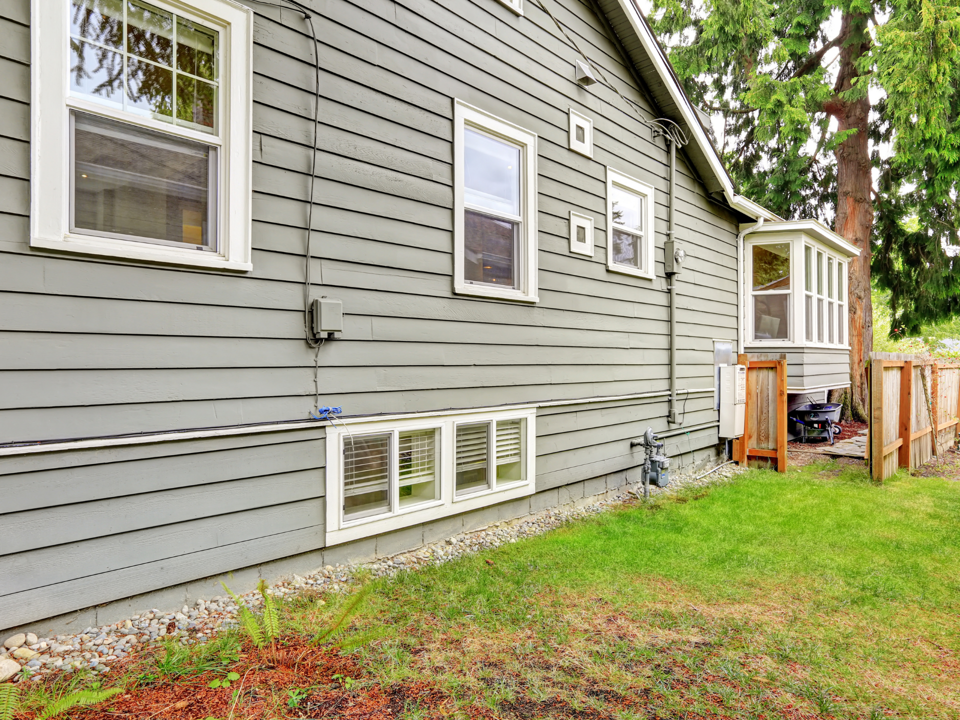 Two-story gray house with black shutters, white garage doors, and a blue sky with clouds.