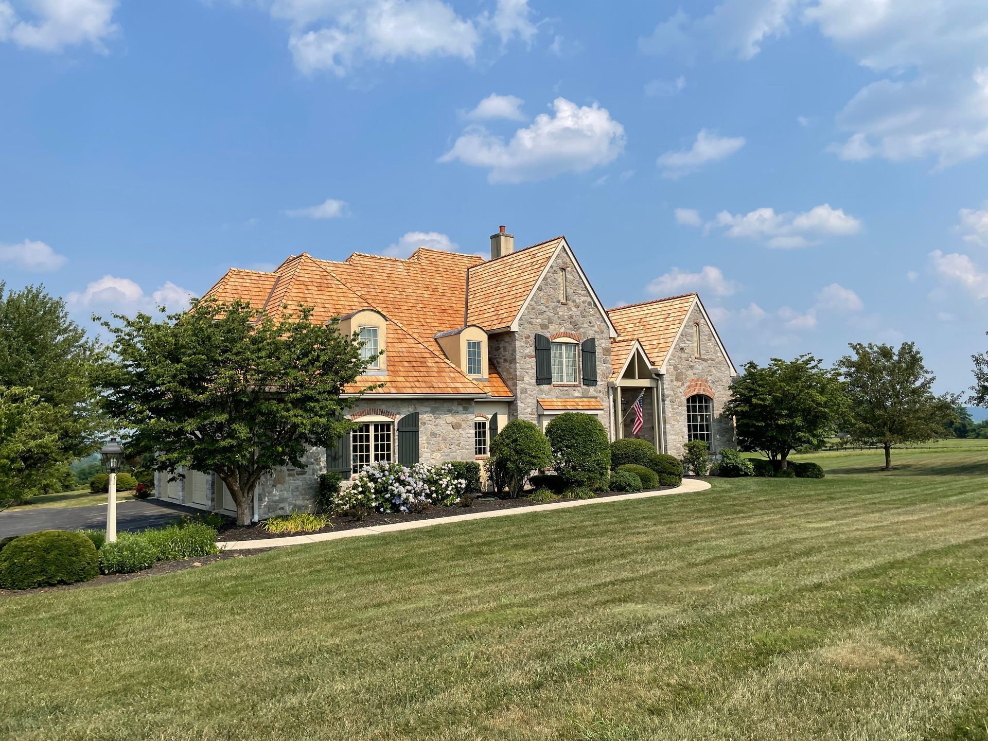 House with stone facade and partially replaced wood shake roof on a sunny day.