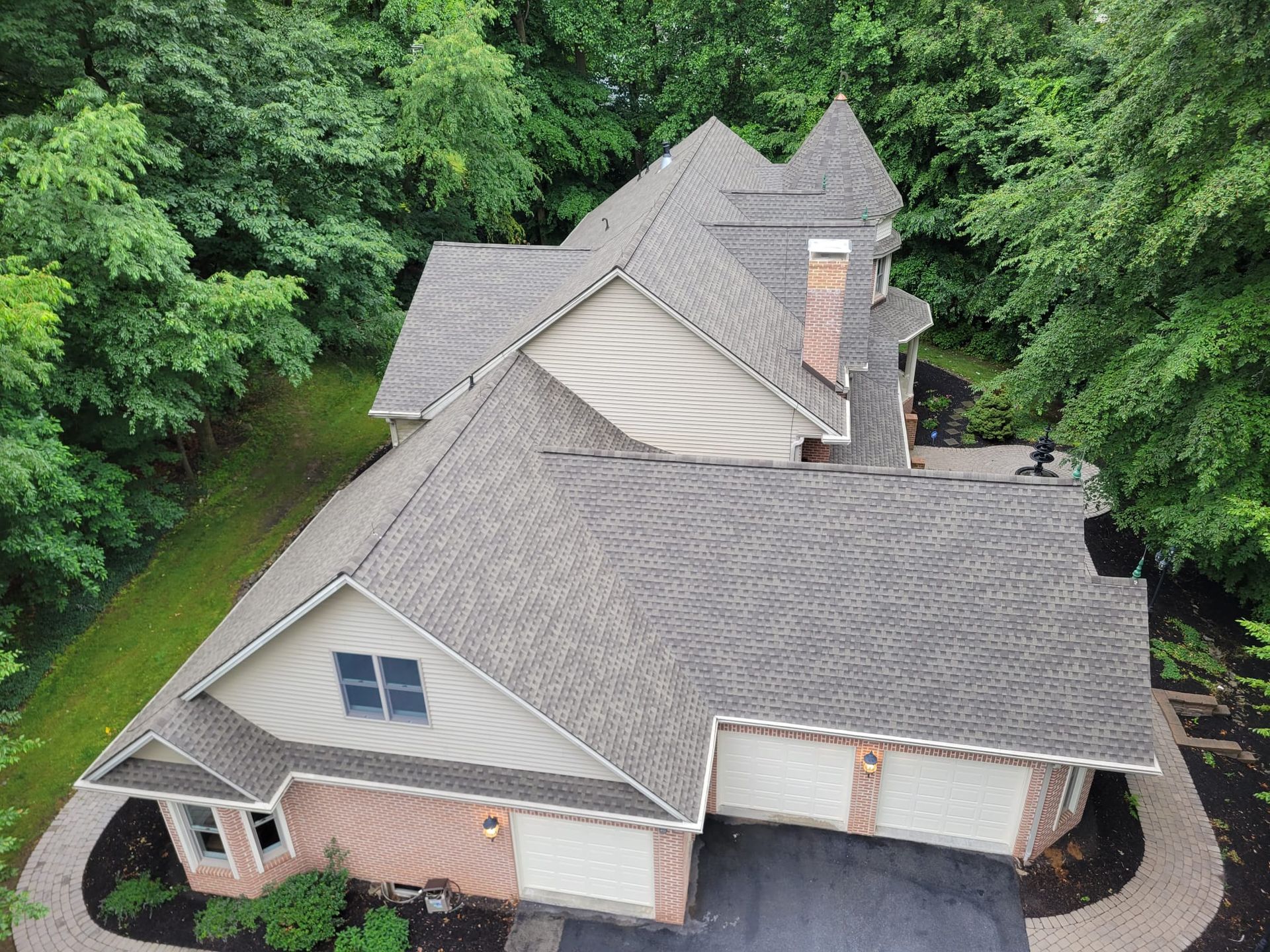 Overhead view of a house with multiple roof sections, surrounded by trees and a driveway.