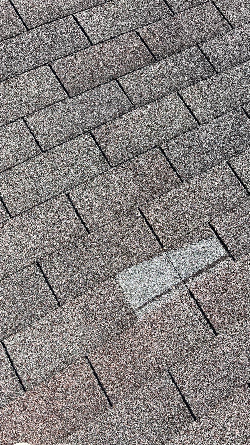 Close-up of asphalt shingle roof; one shingle is missing, revealing the underlying layer.