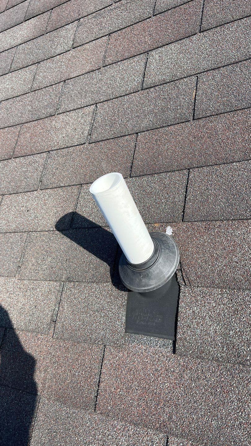 White vent pipe extending from a black base on a brown shingle roof.