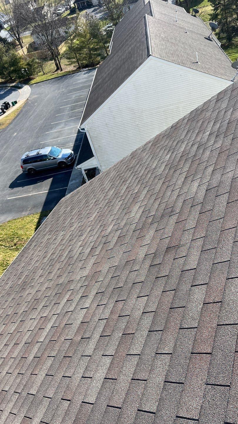 Overhead view of rooftops with asphalt shingles, driveway, and parked car.