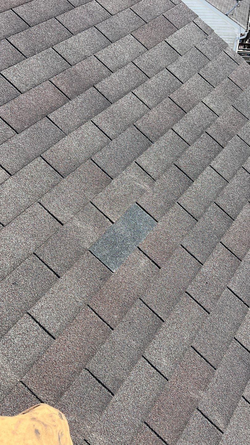 Close-up of a shingled roof with a single, darker-colored shingle replacement.