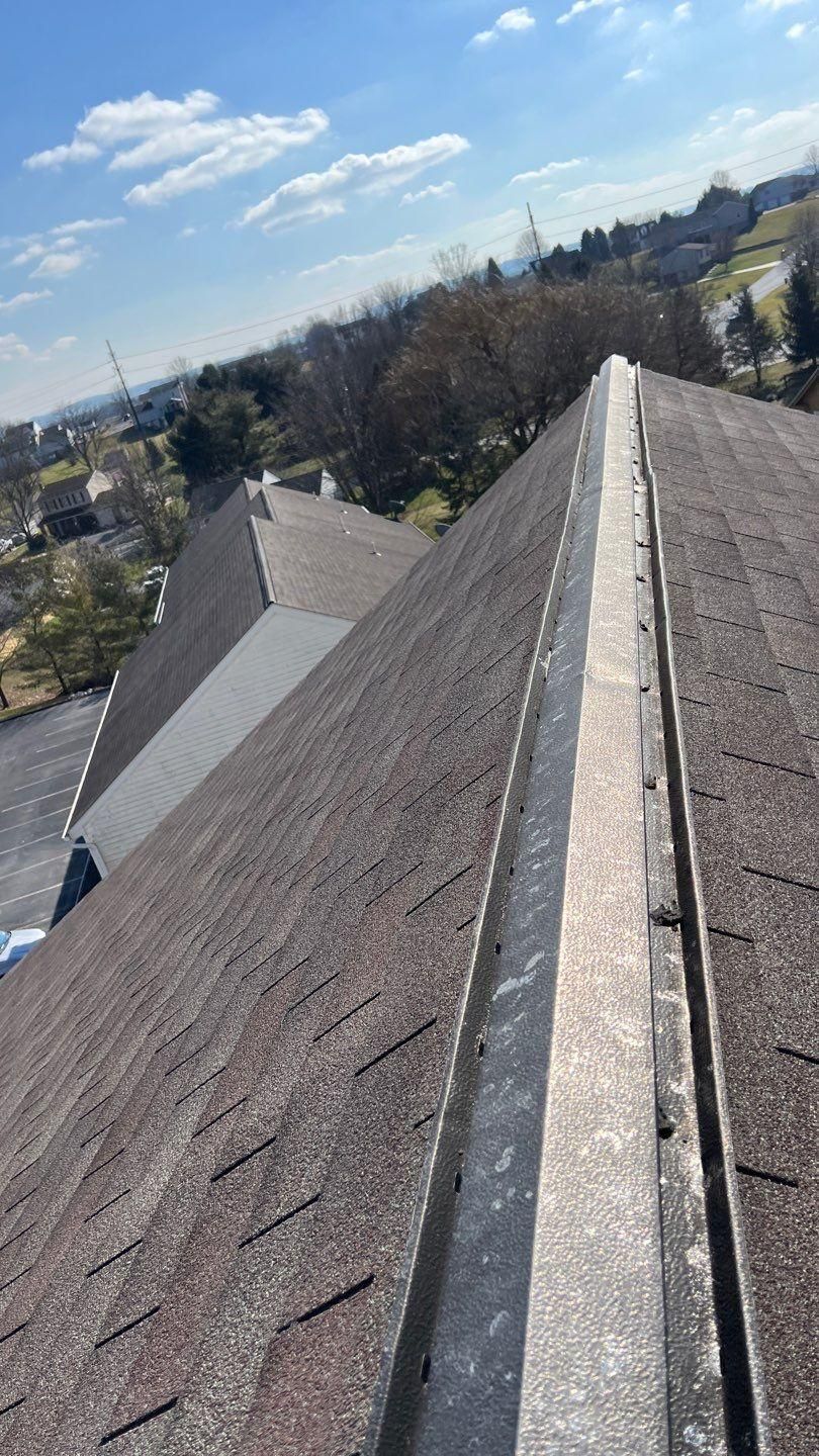 A rooftop with a metal valley and dark-brown shingles, set against a town landscape.
