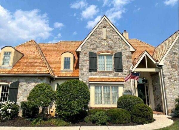 Stone house with wooden shingle roof, dark shutters, and American flag on a sunny day.
