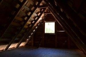 Dark attic interior with wooden beams and a window letting in light.