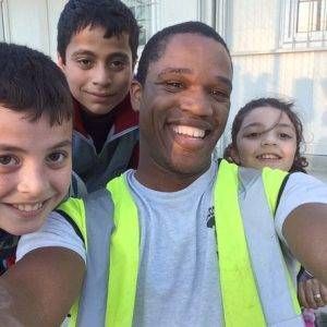 Smiling man in a reflective vest with three smiling children outdoors.
