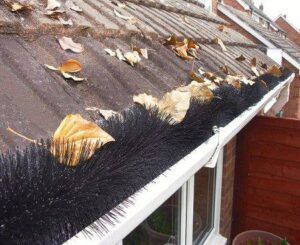 Leaves on a rooftop gutter with a black brush-like gutter guard installed.