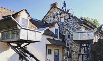 House exterior with two lift platforms attached, workers on roof, ladders.