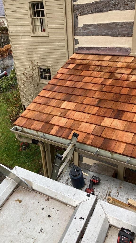 Roof with red-brown shingles, partially covering a wooden structure. Gutters and a ladder visible.