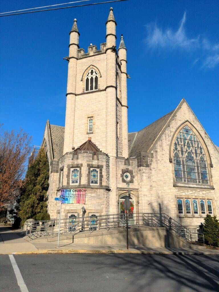 Stone church with a tall tower and stained-glass window under a clear blue sky.