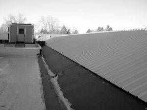 Black and white view of a flat rooftop with a raised HVAC unit and a curved metal roof section.