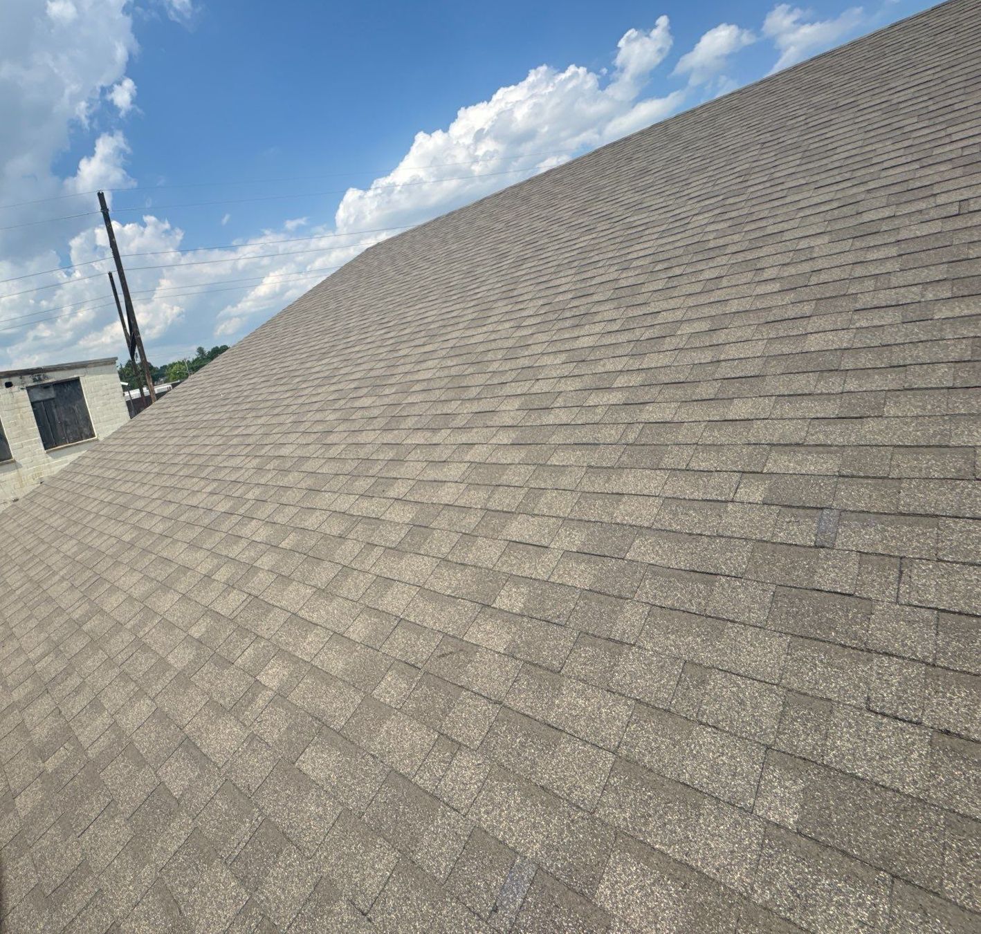 Brown shingle roof under a blue sky with fluffy white clouds, partial view of building.