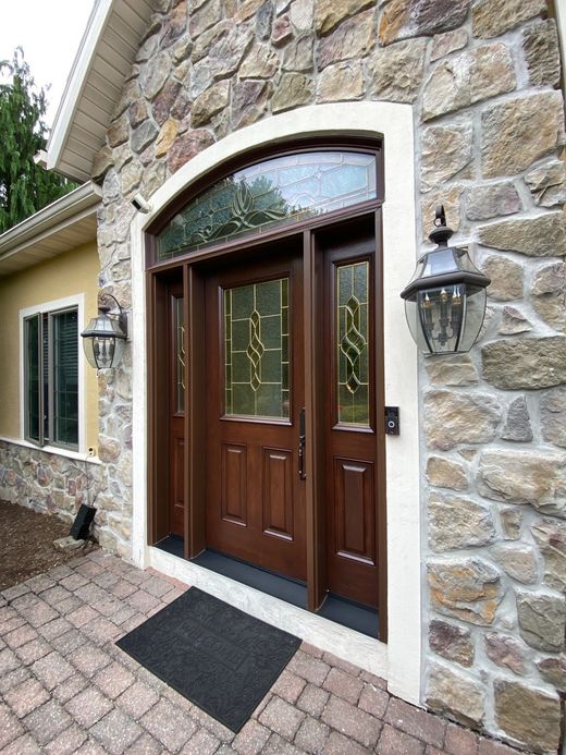 A dark wood front door with sidelights and arched transom, set in a stone facade. Two lantern lights flank the door.