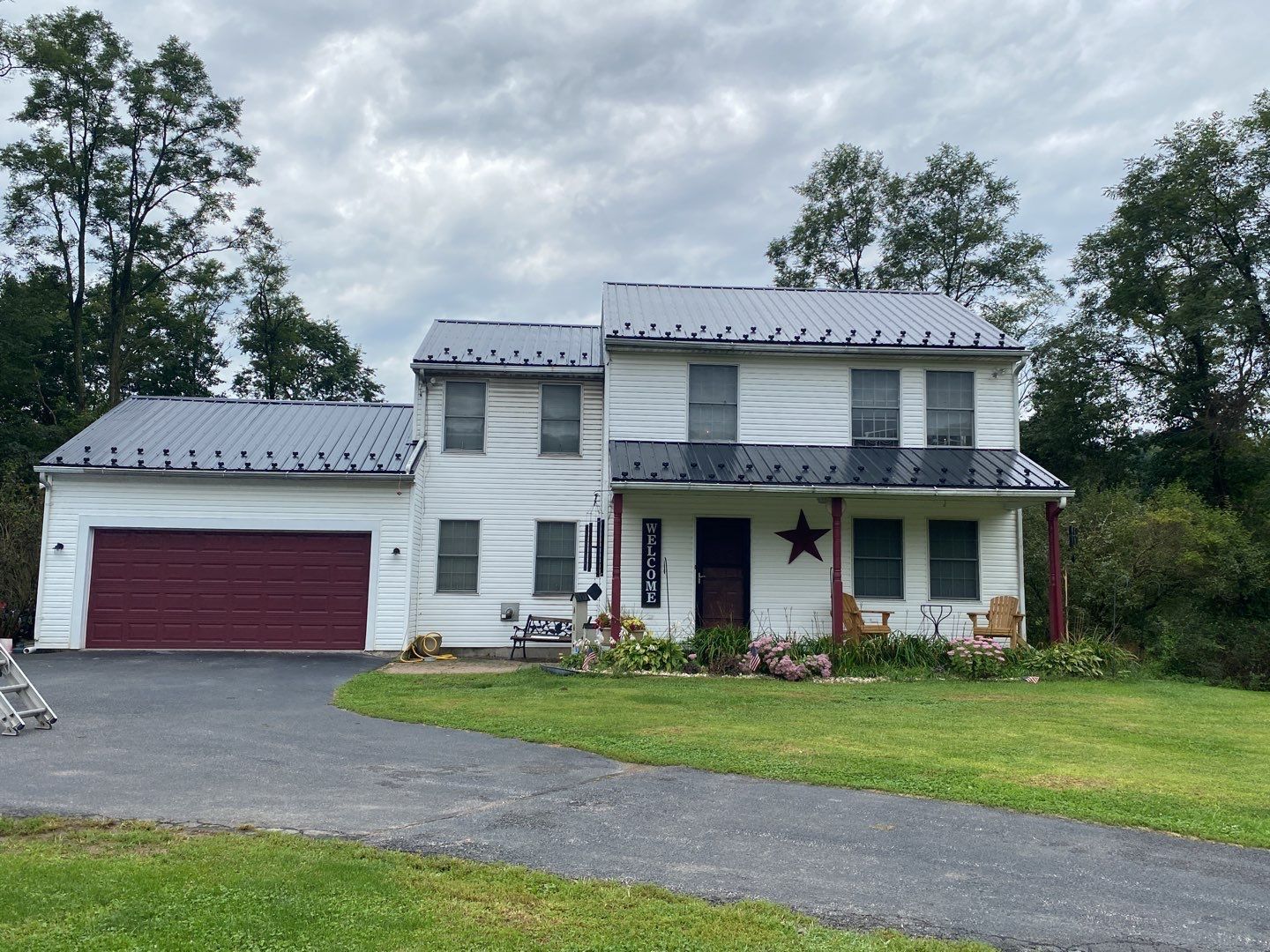 White two-story house with red garage door and roof. Porch with red posts, star decor, on a cloudy day.