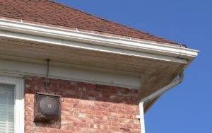 Red brick house corner with white gutters, brown roof, and blue sky.