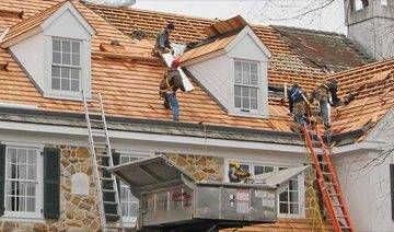 Roofers repairing a house roof with new shingles; workers use ladders and a lift.
