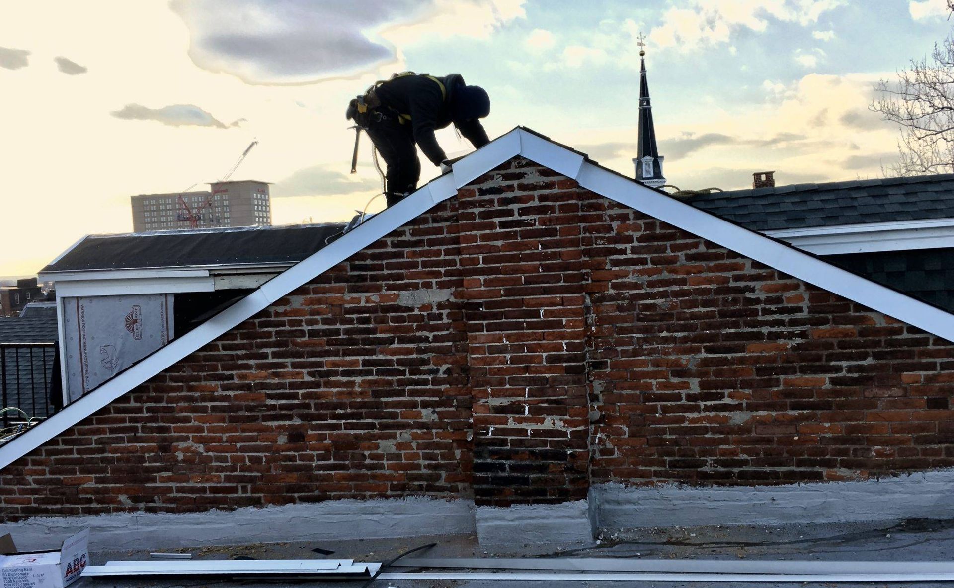 Roofer working on a brick building's gable roof; silhouette against a cloudy sky.