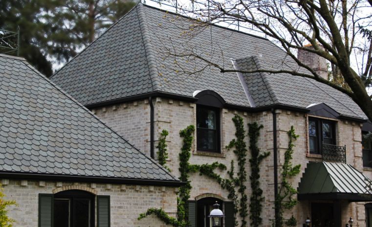 Stone house with gray tiled roof, ivy, and black window frames.