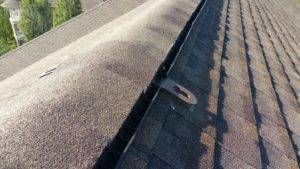 Close-up of a roof showing shingles and a dark valley, likely a gutter, with a metal attachment.