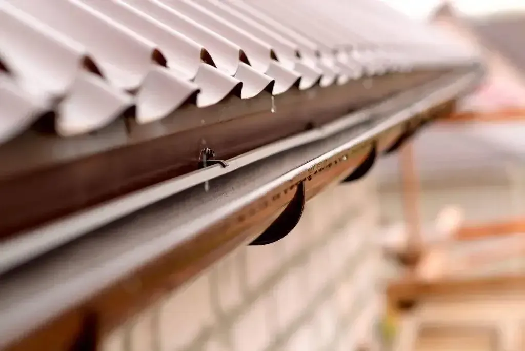 Brown roof gutter with water droplets, attached to a brick building.