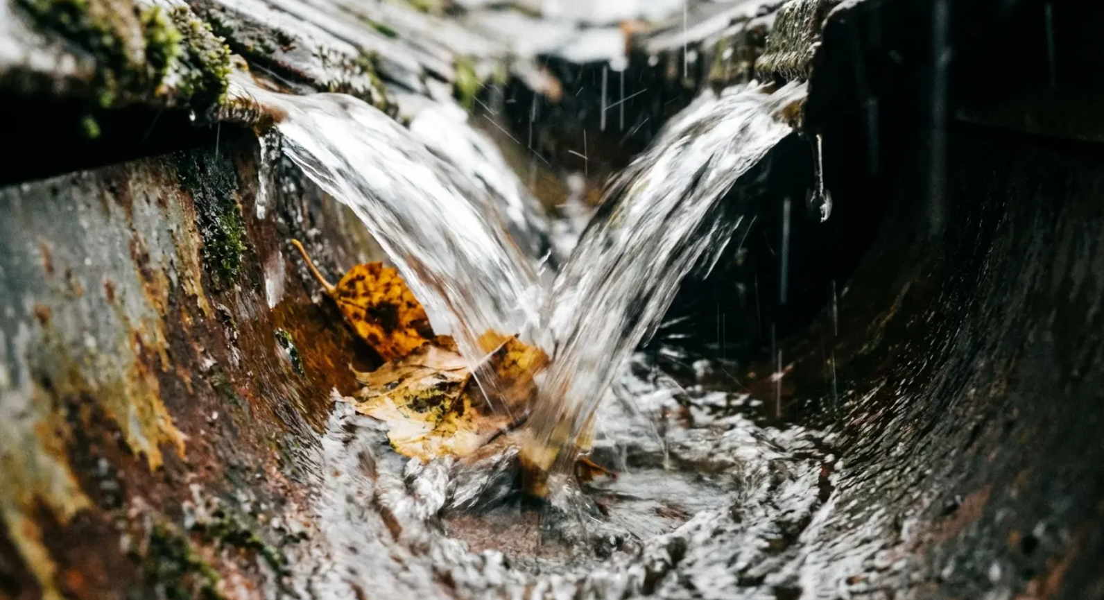 Water cascading into a rusty, angled drain. Brown, decaying matter is visible.