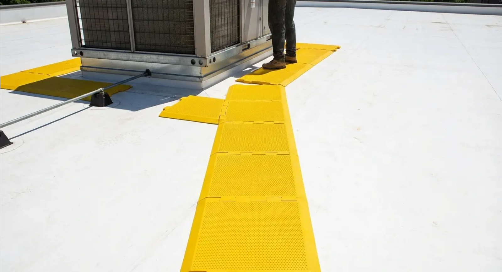 Yellow rooftop walkway around HVAC unit. Person stands on walkway on white roof.
