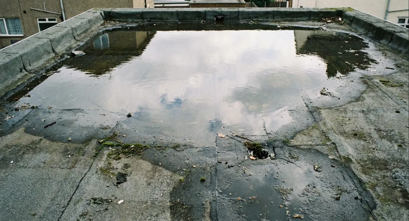 Flat rooftop with standing water reflecting the sky and nearby buildings.
