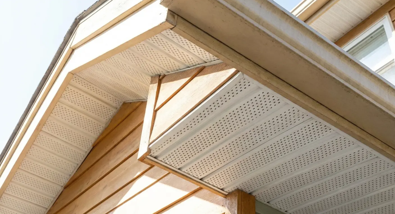 Beige soffit and fascia on a house with a wooden siding, showing ventilation.