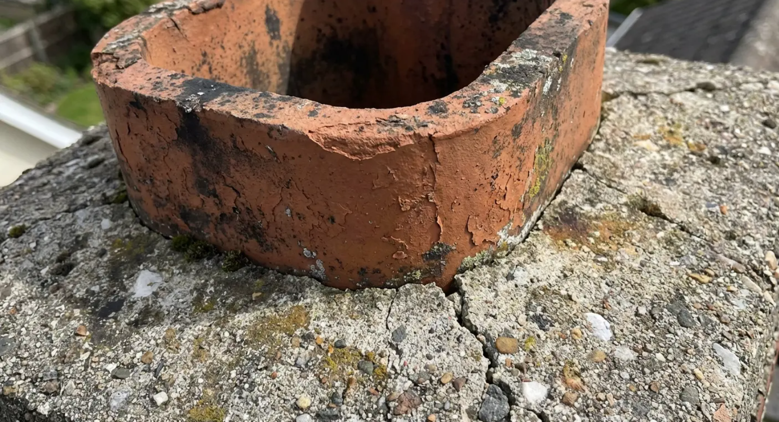 Close-up of a damaged brick chimney cap on a weathered concrete structure.