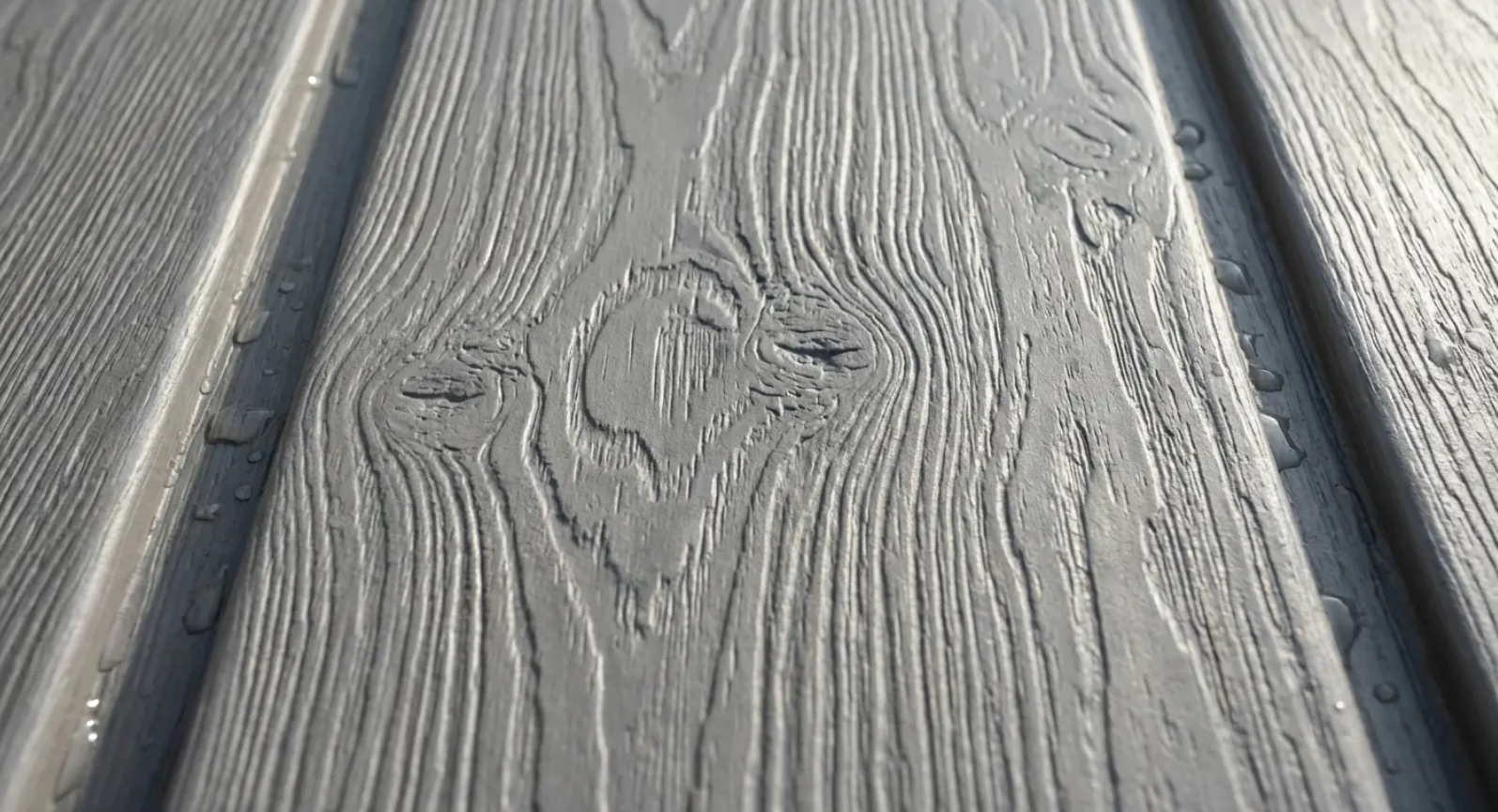 Gray wood-look siding with textured grain, featuring a knot and grooves, possibly outdoors.
