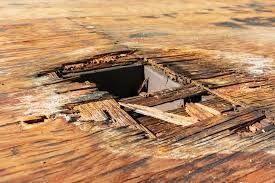 Hole in deteriorating wooden surface, surrounded by broken planks.