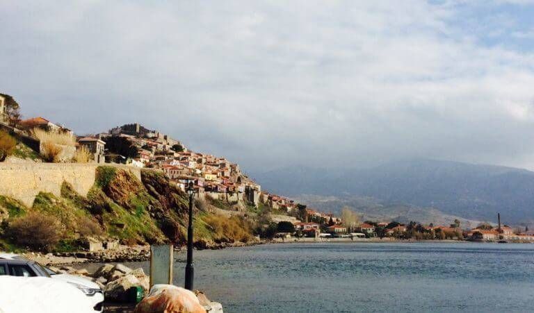 Lakeside village on a hillside with buildings, sea, and cloudy sky.