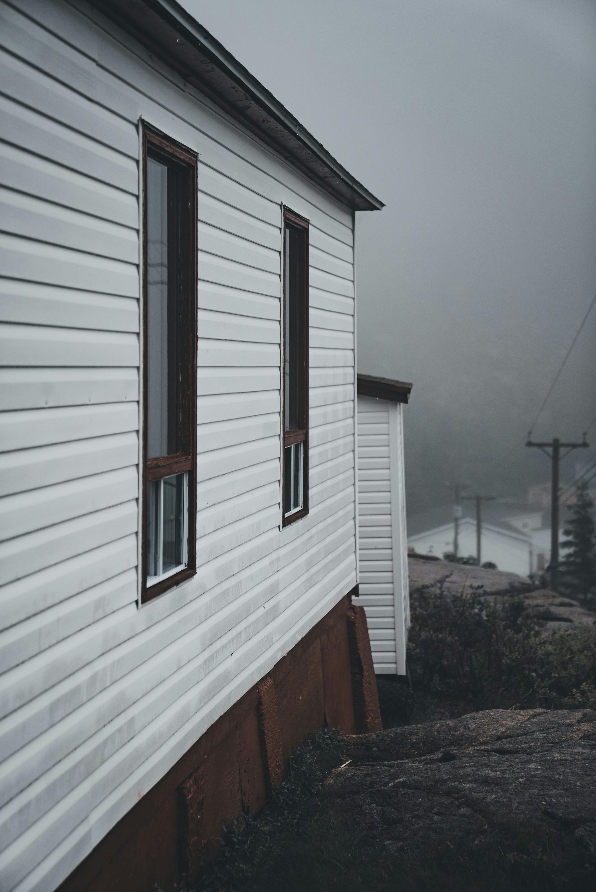 White house siding beside a foggy gravel path with a red foundation