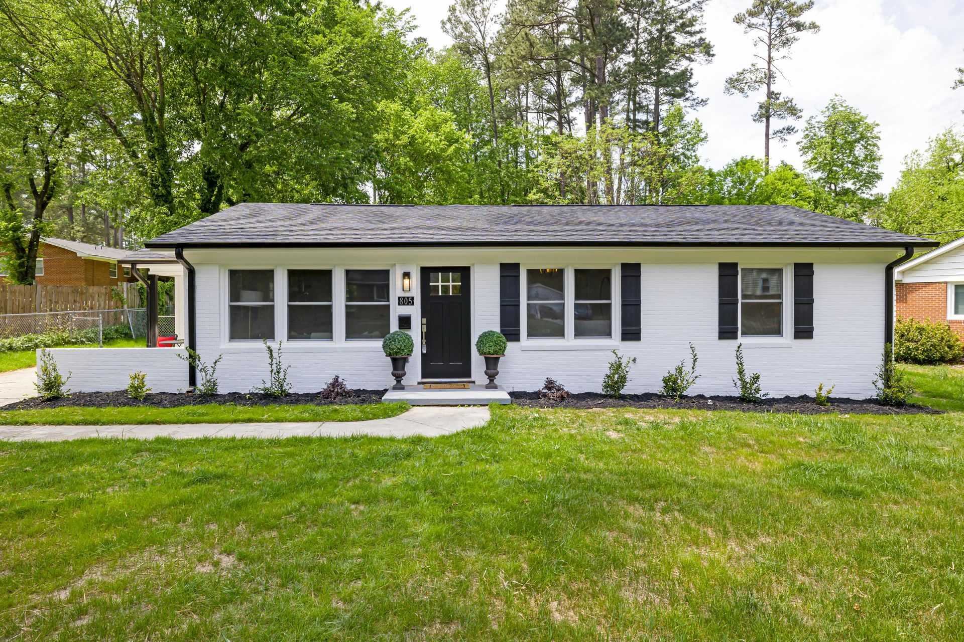 A single-story white house with a black roof, black shutters, and a central black front door, set on a grassy lawn.