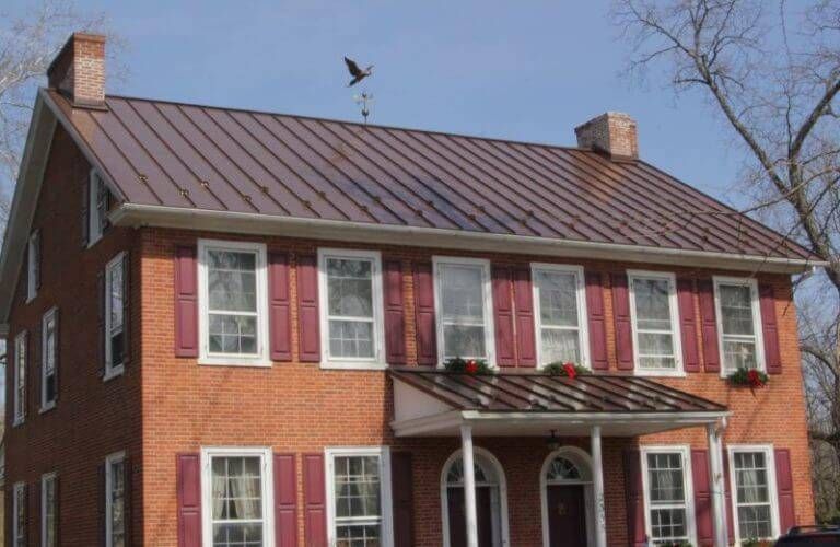 Red brick house with a brown metal roof, red shutters, and a front porch.