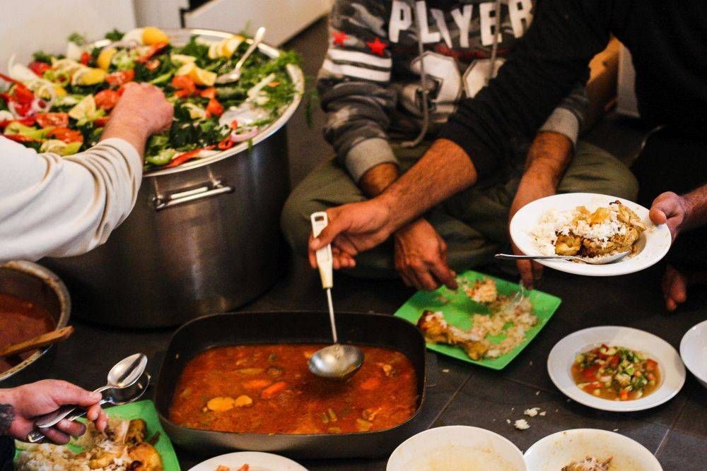 People serving food from large pots onto plates, communal meal setting.