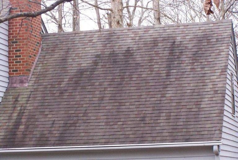 Dark stained asphalt shingle roof on a house, with a brick chimney and white siding.