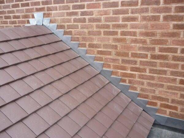 Brown tiled roof with metal flashing meets red brick wall.