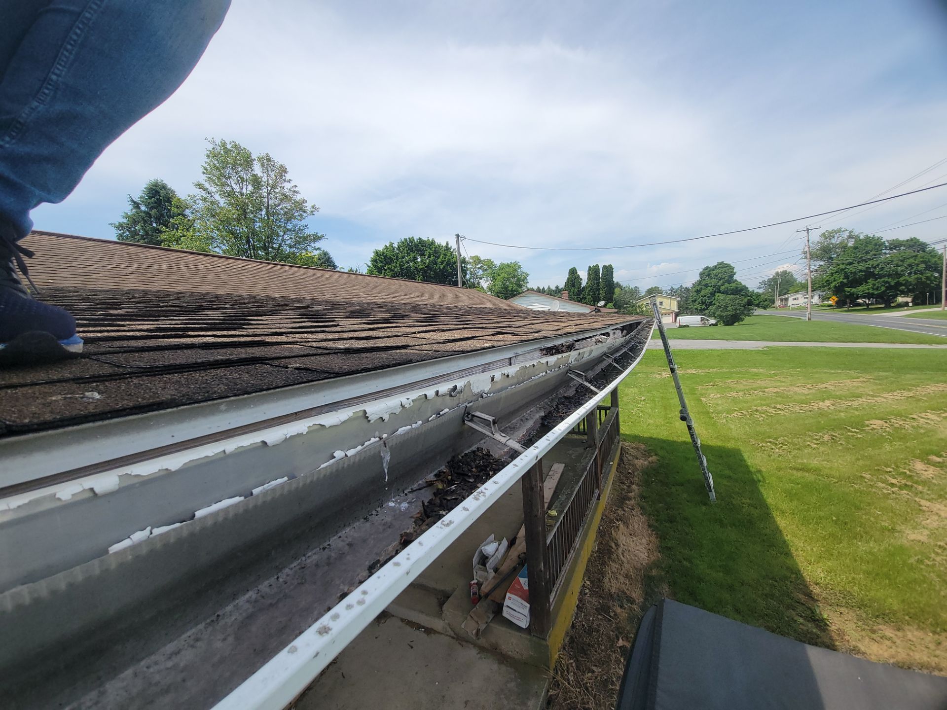 Technician inspecting and cleaning clogged seamless gutters while checking fascia condition on a home in Jonestown, PA.