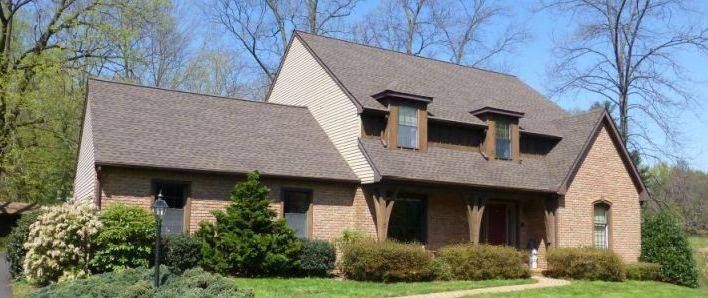 Brick house with brown roof, dormers, and green bushes against a blue sky.