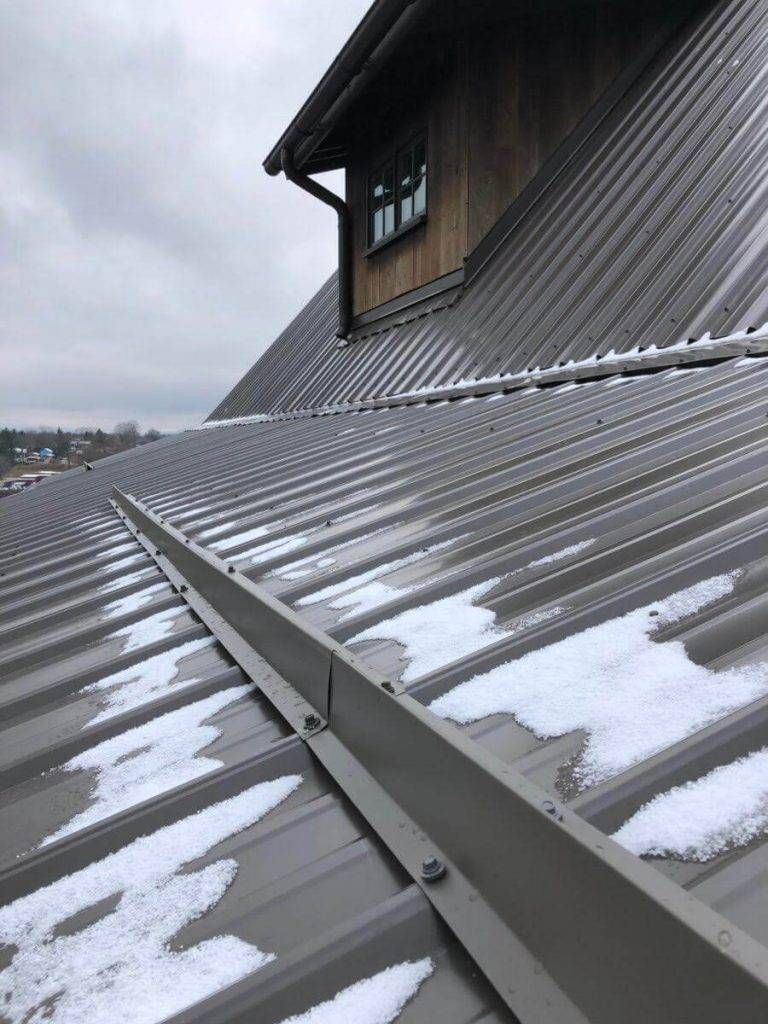Gray metal roof with snow, against a cloudy sky. A wooden dormer sits on top.