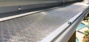 Close-up of a gutter with a screen mesh. Light reflects off the mesh and gutter edge.