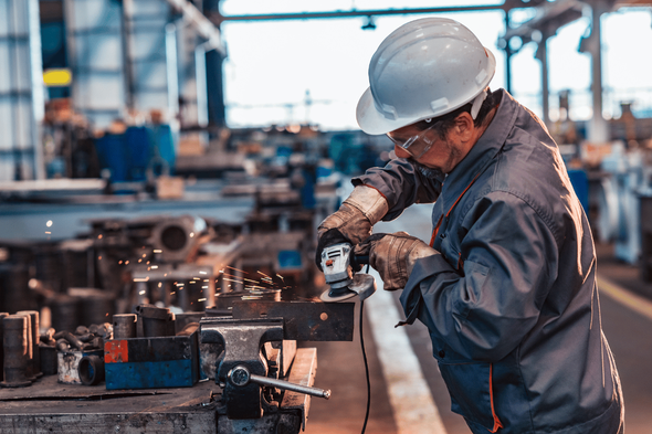 A man wearing a hard hat and safety glasses is working on a machine in a factory.