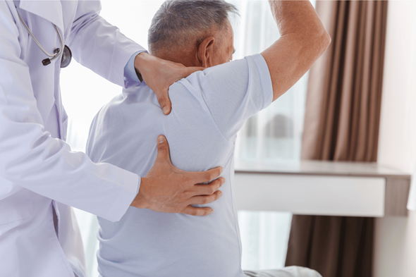 A doctor is examining an older man 's back and shoulder.