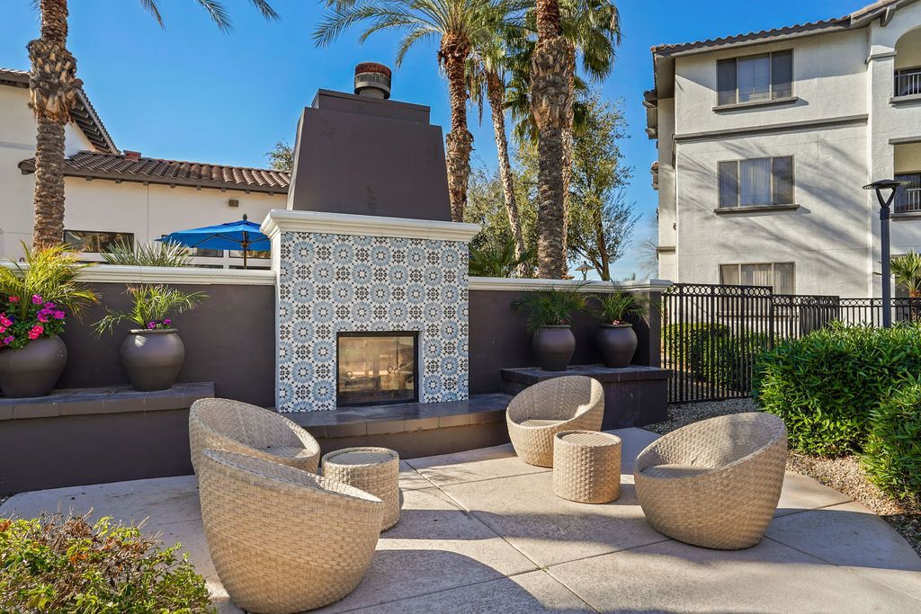 Outdoor communal seating area with a tiled fireplace, wicker chairs, and potted plants.