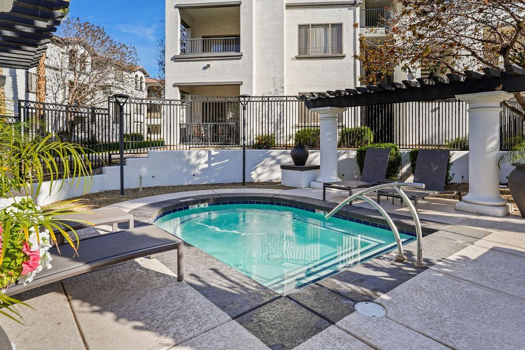 Outdoor pool area with lounge chairs and a metal fence at an apartment community.