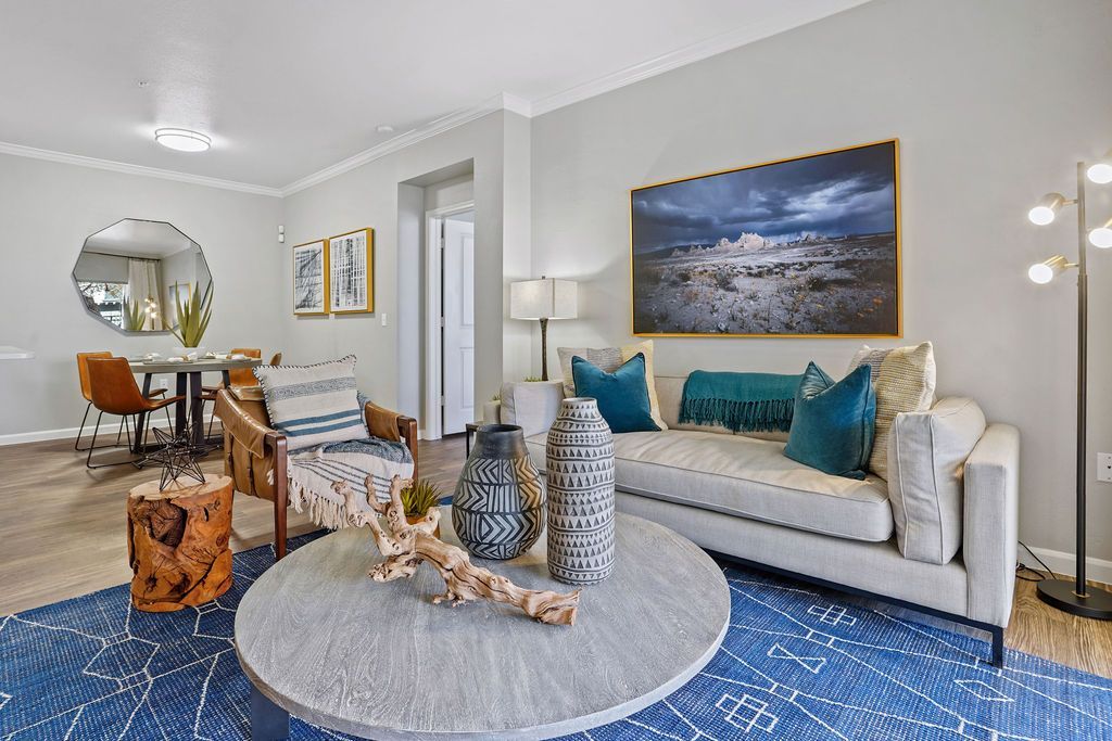 Living room in a modern apartment with a beige sofa, teal pillows, and round coffee table.